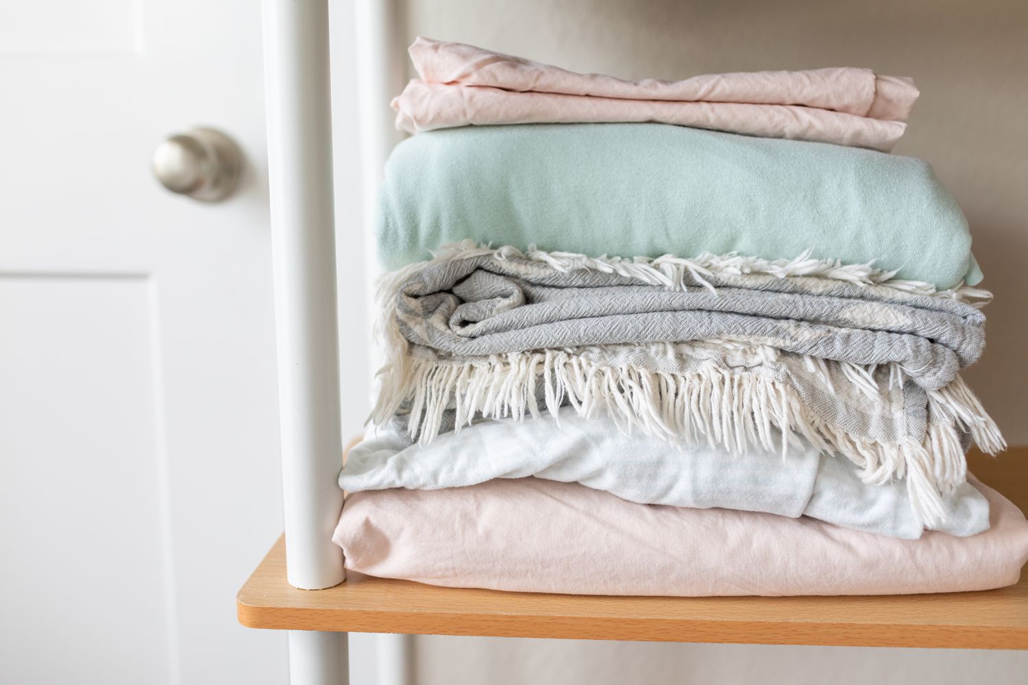 neatly folded pastel bed sheets sit on open storage rack next to white door