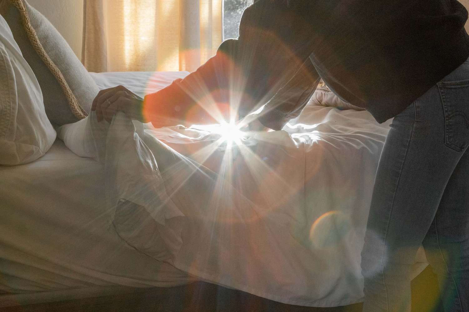 person makes bed while sunlight from window makes high beam on camera