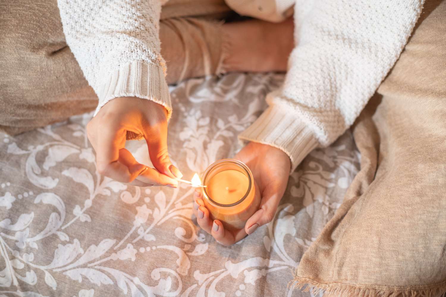 woman lights beeswax candle on bed