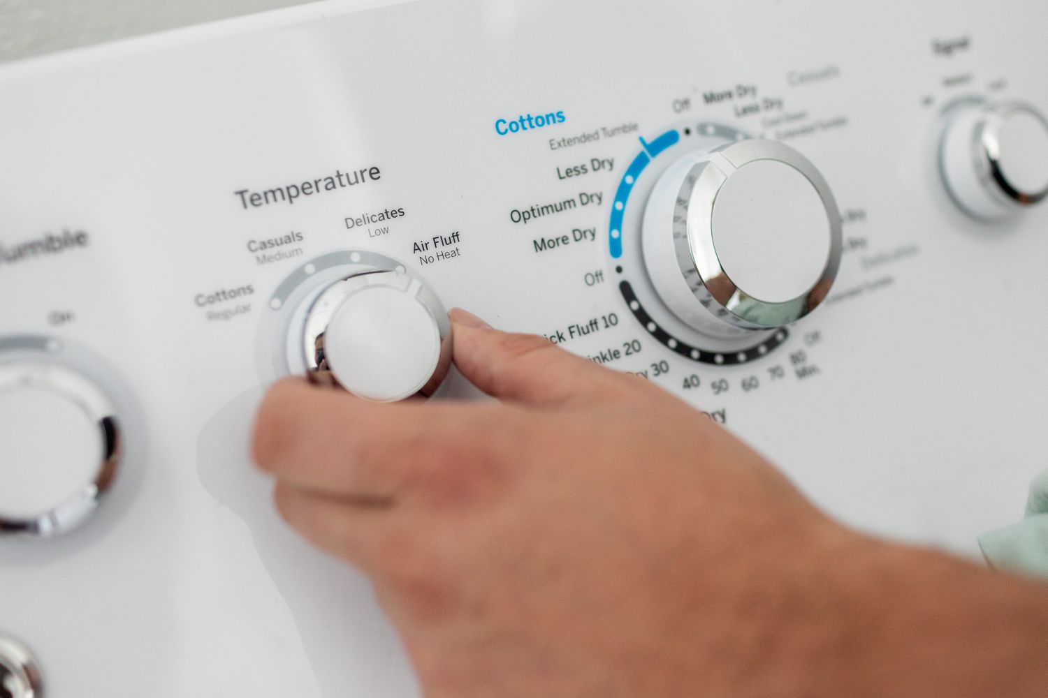 hand turns dial on clothing dryer to air fluff option for pillows