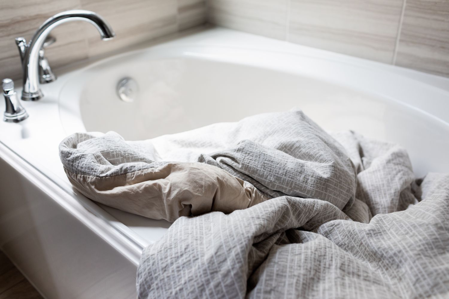 cleaning a fluffy striped duvet in a large, deep white bathtub 